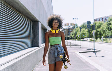 Lächelnde junge Frau mit Skateboard auf dem Gehweg - OIPF02433