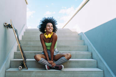Glückliche junge Frau, die auf einer Treppe neben einem Skateboard sitzt - OIPF02444