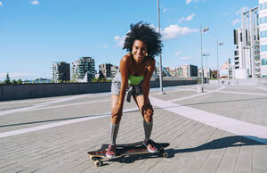 Glückliche junge Frau steht auf einem Skateboard in der Stadt - OIPF02455