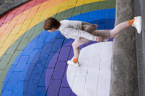 Junge Frau, die auf eine regenbogenfarbene Wand tritt - AMWF00952