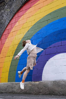 Junge Frau springt vor einer regenbogenfarbenen Wand - AMWF00970