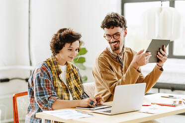 Zufriedener Illustrator mit einem Kollegen, der ein Grafiktablett und einen Laptop am Schreibtisch benutzt - MDOF00057