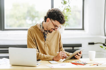 Happy illustrator wearing eyeglasses using digital tablet at desk - MDOF00063