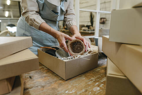 Hände einer Handwerkerin verpacken Häkeldekor in einer Schachtel auf einer Werkbank - YTF00301