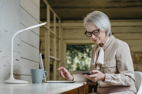 Geschäftsfrau schaut auf Tablet-PC mit Laptop am Schreibtisch im Büro sitzend - YTF00311