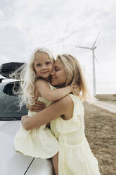 Smiling woman hugging daughter sitting on car hood - SIF00520