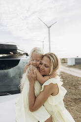 Smiling woman embracing daughter sitting on car hood - SIF00521