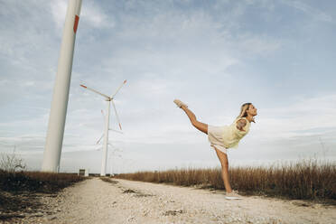 Woman standing with arms outstretched by wind turbines on field - SIF00528