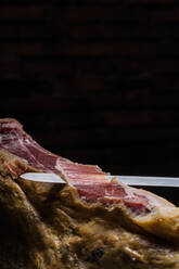 Crop unerkennbar Koch Schneiden Scheibe von leckeren trocken gepökelt spanischen Jamon auf schwarzem Hintergrund - ADSF39620