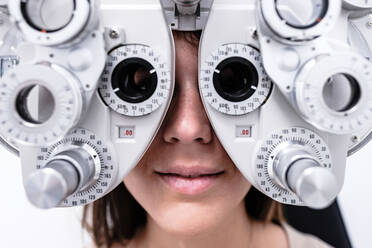Smiling female patient in modern phoropter checking vision during visit in modern ophthalmological clinic - ADSF39640