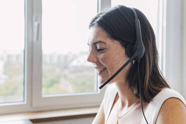 Happy young customer service representative with freckles on face wearing headset in office - PNAF04609