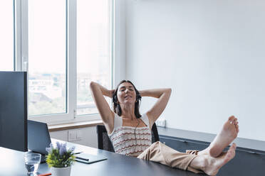 Relaxed young customer service representative wearing headset relaxing in office - PNAF04612