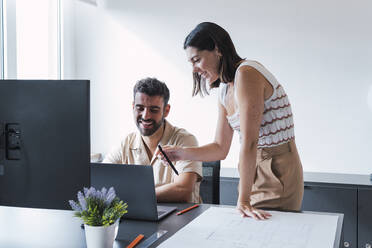 Fröhliche Kollegen, die im Büro am Laptop diskutieren - PNAF04617