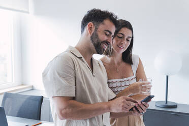 Smiling businessman sharing smart phone with businesswoman in office - PNAF04620