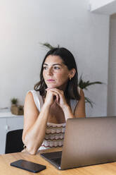 Contemplative young businesswoman sitting in front of laptop at office - PNAF04630