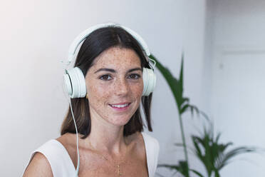 Lächelnde junge Frau, die im Büro über Kopfhörer Musik hört - PNAF04658