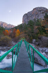 Schmale Fußgängerbrücke über einen schnellen Gebirgsfluss im herbstlichen Sonnenuntergang im Nationalpark Ordesa y Monte Perdido in Huesca, Spanien - ADSF39702