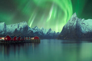 Spektakulärer Blick auf lebendige grüne Polarlichter, die am Himmel über Wohnhäusern im Hochland in der Nähe eines Sees in Norwegen bei Nacht leuchten - ADSF39738