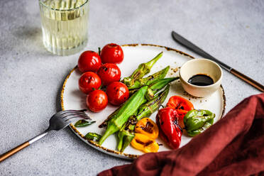 Gesundes Abendessen mit gegrillter Bamia, Paprika und Kirschtomaten mit Soja- und Balzamico-Saucen, serviert mit einem Glas kaltem, trockenem Wein - ADSF39790