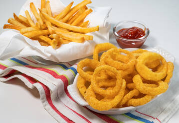 Fried onion rings and French fries with ketchup on tablecloth - TETF01812