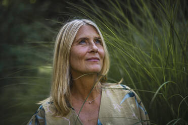 Nachdenkliche reife Frau mit blondem Haar im Garten - RIBF01085