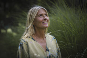 Smiling thoughtful mature woman in blond hair at garden - RIBF01087