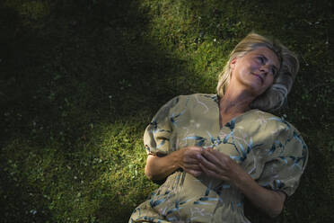 Mature woman lying on grass  in garden - RIBF01101