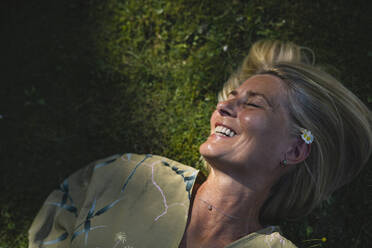 Happy mature woman lying on grass enjoying sunlight - RIBF01104
