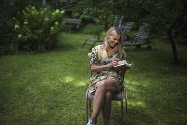 Glückliche reife Frau liest Buch im Garten - RIBF01108