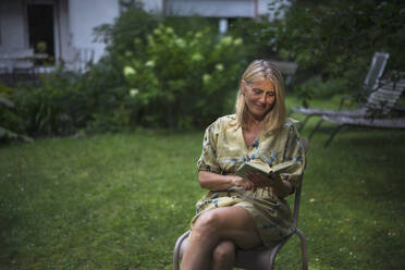 Lächelnde reife Frau liest Buch im Garten - RIBF01109