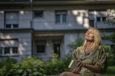 Ältere Frau mit Buch entspannt im Garten - RIBF01110