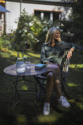 Woman sitting on chair in front yard of house - RIBF01120