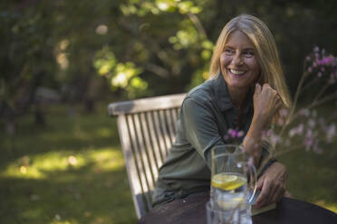 Glückliche reife Frau mit blondem Haar sitzt im Garten - RIBF01121