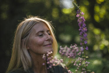 Smiling woman looking at flowering plant in garden - RIBF01132