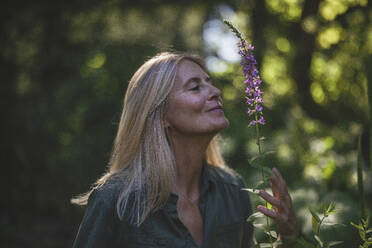 Ältere Frau riecht an einer Blume im Garten - RIBF01135