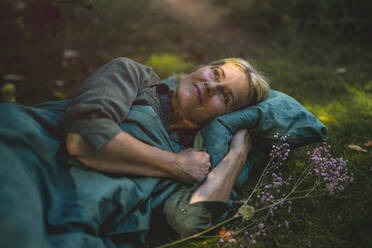 Thoughtful mature woman lying on grass in garden - RIBF01152