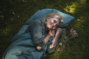 Smiling mature woman lying on grassy area in garden - RIBF01153