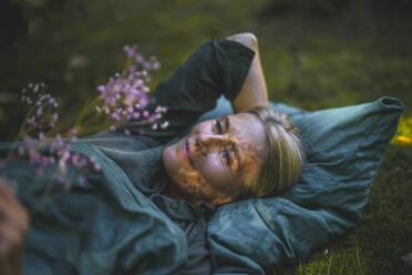 Thoughtful mature woman lying in garden - RIBF01159