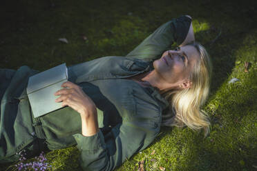 Contemplative woman lying on grass in garden - RIBF01171