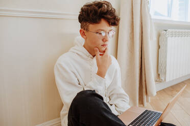 Junge mit Händen am Kinn beim E-Learning am Laptop - MDOF00080
