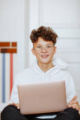 Smiling boy sitting with laptop at home - MDOF00100