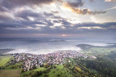 Deutschland, Baden-Württemberg, Drohnenaufnahme von Wolken über einem Dorf im Remstal bei nebligem Herbstsonnenaufgang - STSF03568