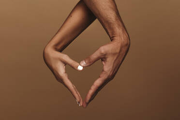 Couple making heart shape with hand against brown background. Close up of man and woman hands making a heart shape symbol. - JLPSF11378