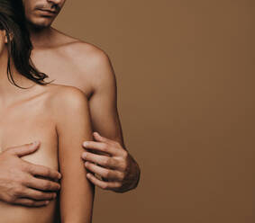 Mann hält Frau von hinten auf braunem Hintergrund. Sinnliches junges Paar mit nacktem Körper. - JLPSF11382