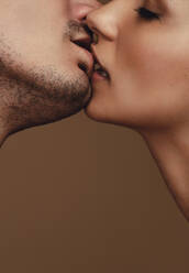 Nahaufnahme eines jungen Paares, das sich leidenschaftlich küsst. Zärtlicher Mann und Frau, die sich auf braunem Hintergrund küssen. - JLPSF11391