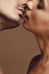 Nahaufnahme eines jungen verliebten Paares, das sich auf braunem Hintergrund küsst. Sinnliches junges Paar beim Küssen. - JLPSF11392