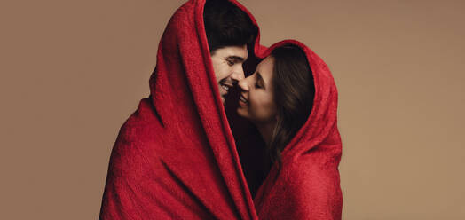 Liebevolles junges Paar unter einer roten Decke, das sich küsst. Glücklicher junger Mann und Frau, die eine schöne Zeit miteinander verbringen. - JLPSF11396