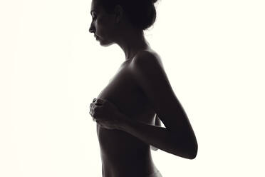 Silhouette of sensual woman standing naked against white background. Side view of female covering her breast with hand. - JLPSF11408