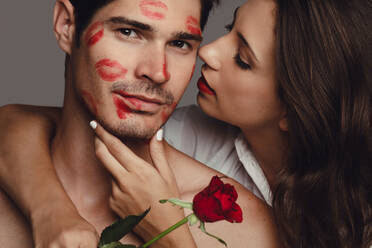 Close up of woman kissing her boyfriend. Man kissed by girlfriend with lipstick kiss marks on the face. - JLPSF11413
