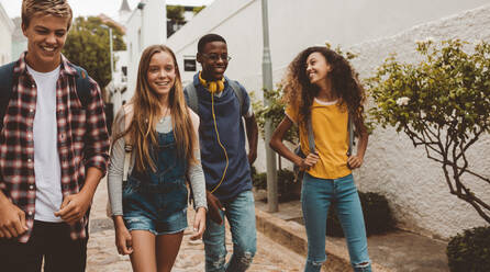 Multiethnic college friends walking in street. Happy boys and girls walking in street wearing college bags. - JLPSF11439